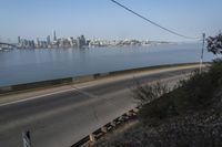 a road passing along a body of water with a city skyline in the background from an elevated view