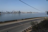 a road passing along a body of water with a city skyline in the background from an elevated view