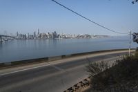 a road passing along a body of water with a city skyline in the background from an elevated view