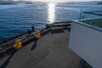 the view of a calm blue ocean and the sun reflecting on the water from the bow of a large boat