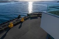 the view of a calm blue ocean and the sun reflecting on the water from the bow of a large boat