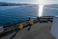 the view of a calm blue ocean and the sun reflecting on the water from the bow of a large boat