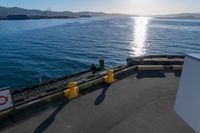 the view of a calm blue ocean and the sun reflecting on the water from the bow of a large boat