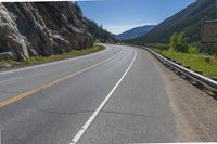 the highway that runs into a valley with mountains and trees on it and green grass on either side