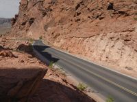 a motorcycle rider rides through a narrow valley on the road between high cliffs and dry grass