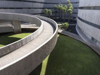 a circular green lawn and concrete walkway with a round shaped building and trees in the background