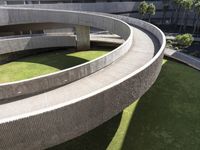 a circular green lawn and concrete walkway with a round shaped building and trees in the background