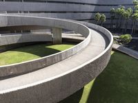 a circular green lawn and concrete walkway with a round shaped building and trees in the background