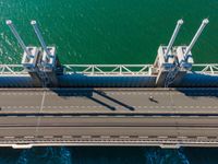 a bridge over the ocean with construction equipment in the background and two people walking on it