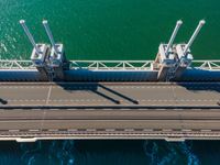 a bridge over the ocean with construction equipment in the background and two people walking on it