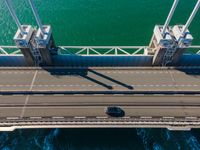 a bridge over the ocean with construction equipment in the background and two people walking on it