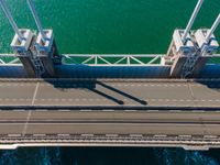 a bridge over the ocean with construction equipment in the background and two people walking on it