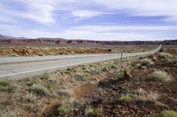 a lone white truck traveling on an empty road through the desert near the mountains,