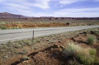 a lone white truck traveling on an empty road through the desert near the mountains,