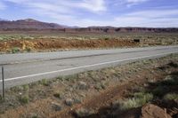 a lone white truck traveling on an empty road through the desert near the mountains,