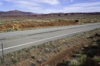 a lone white truck traveling on an empty road through the desert near the mountains,