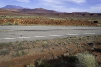 a lone white truck traveling on an empty road through the desert near the mountains,