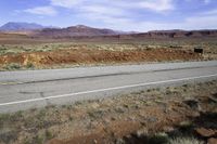 a lone white truck traveling on an empty road through the desert near the mountains,