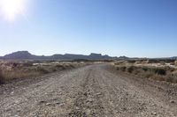 an empty road in a wide open plain of land near mountains and water on a sunny day