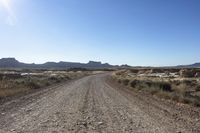 an empty road in a wide open plain of land near mountains and water on a sunny day