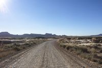 an empty road in a wide open plain of land near mountains and water on a sunny day