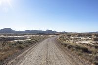 an empty road in a wide open plain of land near mountains and water on a sunny day