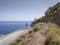 a car drives down the road alongside a rocky cliff on a beach side with blue sea and sky in the background