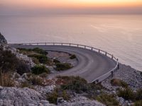 a curving curved curved road on the edge of water near an ocean at sunset time