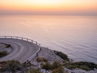 a curving curved curved road on the edge of water near an ocean at sunset time