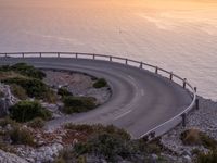 a curving curved curved road on the edge of water near an ocean at sunset time