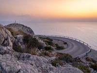 a curving curved curved road on the edge of water near an ocean at sunset time