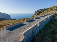 an old cement road and stone structure on grassy hill overlooking the water, blue sky, sea and rocks