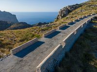 an old cement road and stone structure on grassy hill overlooking the water, blue sky, sea and rocks