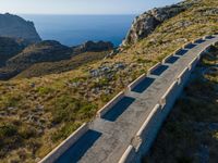 an old cement road and stone structure on grassy hill overlooking the water, blue sky, sea and rocks