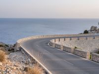 a car is driving down a curvy road on a clear day near the ocean