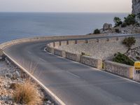 a car is driving down a curvy road on a clear day near the ocean