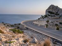 a car is driving down a curvy road on a clear day near the ocean