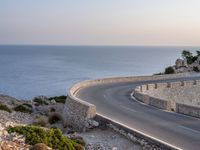 a car is driving down a curvy road on a clear day near the ocean