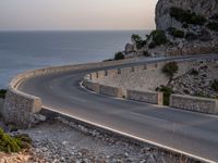 a car is driving down a curvy road on a clear day near the ocean