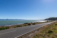 the view of the road along the shoreline from the road near the ocean and mountains