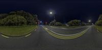 a black road at night with lights on and green grass in the middle of the street