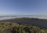 a winding road with mist and a city behind it in the distance on a clear day