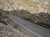 a black and white motorcycle is driving down the winding road on a mountain road near rocks