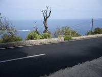 a black paved street with white lines along side an ocean and mountains behind it in front of an ocean