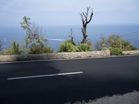 a black paved street with white lines along side an ocean and mountains behind it in front of an ocean
