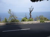 a black paved street with white lines along side an ocean and mountains behind it in front of an ocean