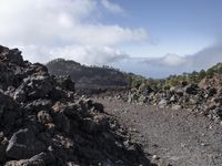 a mountain slope with lava and rocks on the ground, with hills in the background