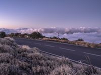 an empty winding road on a mountain with the sun set above the mountains in the background