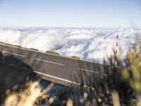 a man rides his motorcycle down the road below clouds as he looks back over the top of a hill