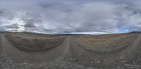 fisheye view of a field with no grass and a road sign, with sky in the background